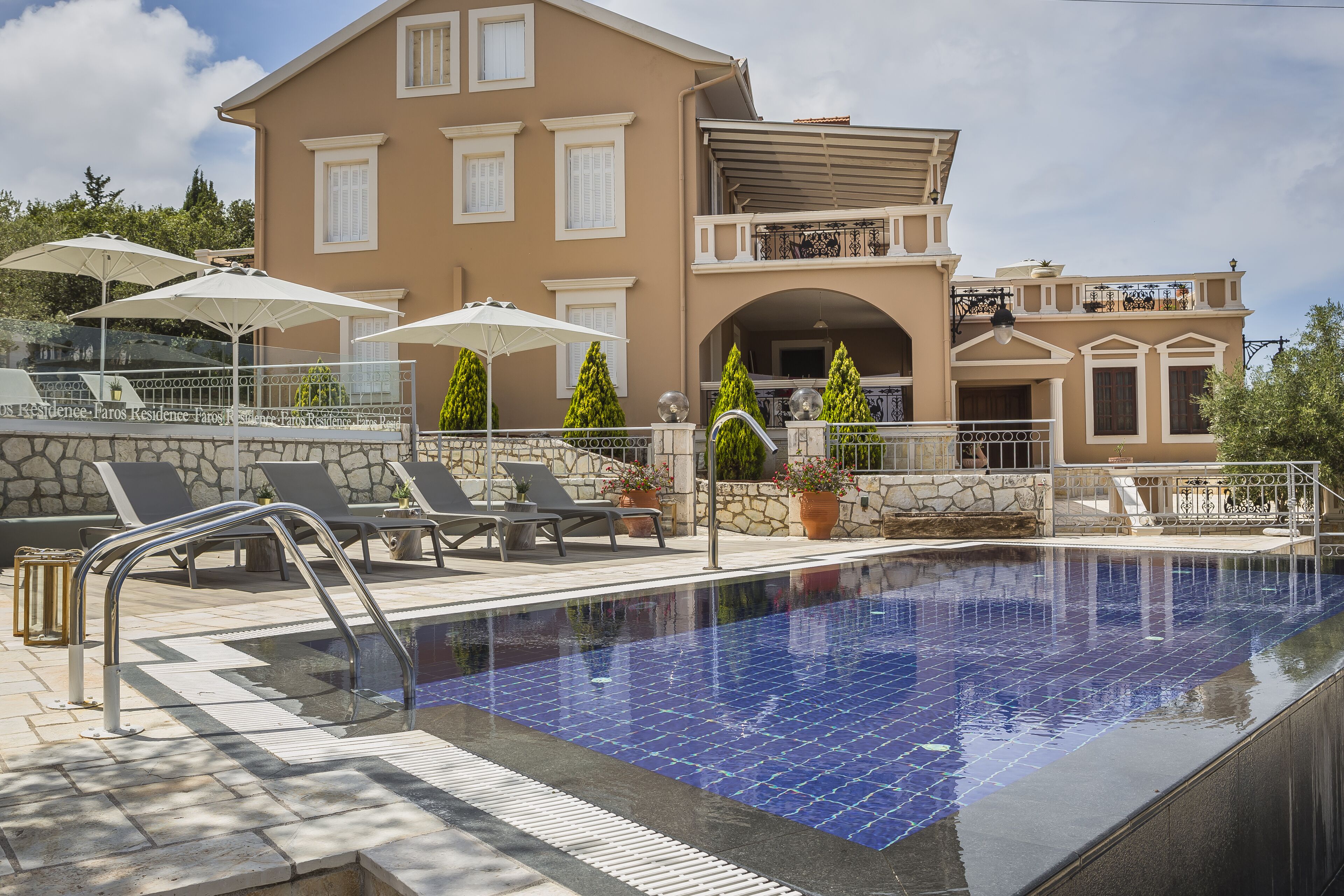Une piscine avec des chaises longues et des parasols, un mur en pierre et un bâtiment à deux étages doté de balcons.