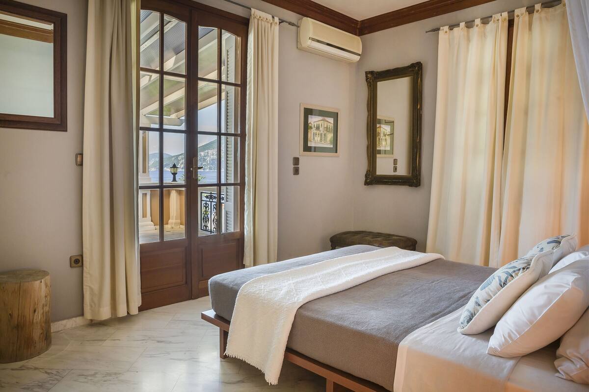 A bedroom with a bed, a large window, a mirror, and a framed picture on the wall.