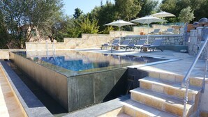 A swimming pool with steps leading down to the water, surrounded by lounge chairs and umbrellas. - Faros Residence - Adults Only (Kefalonia)