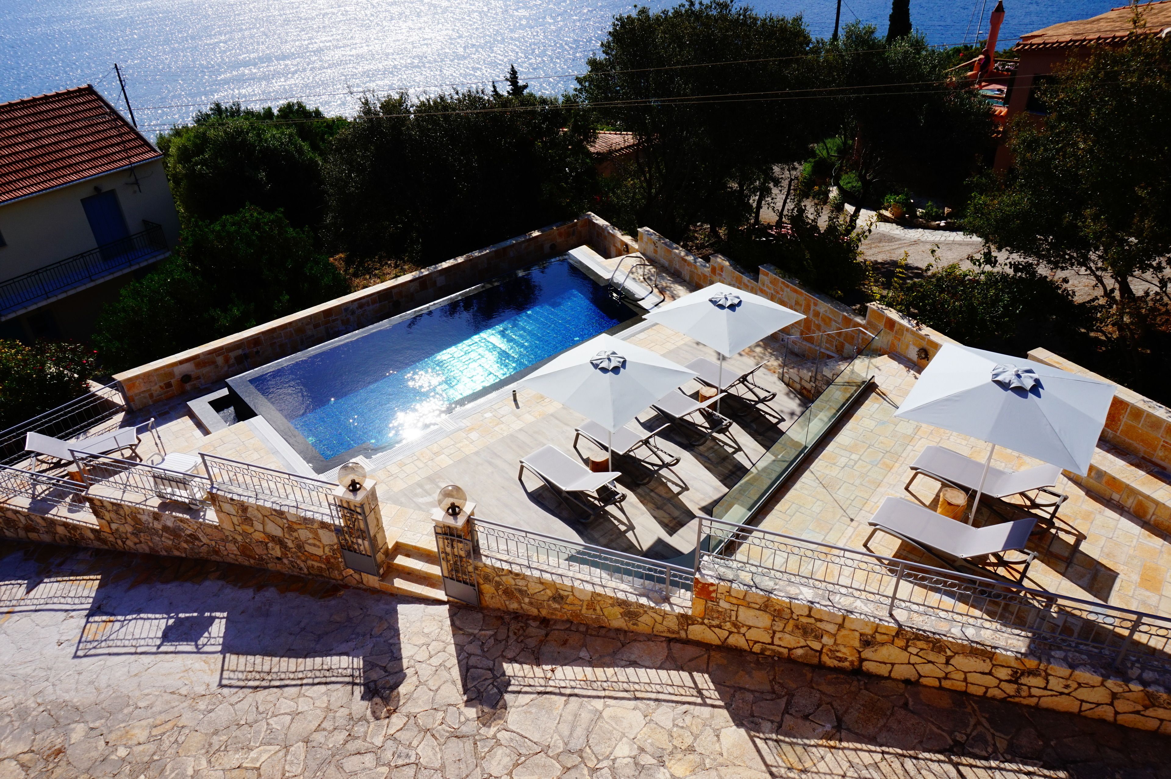 Ein Pool mit Liegestühlen und Sonnenschirmen, umgeben von Steinmauern und Blick aufs Meer.