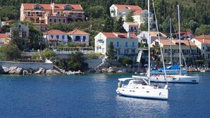 A coastal town with multiple buildings, a marina with sailboats, and a rocky shoreline. - Faros Residence - Adults Only (Kefalonia)