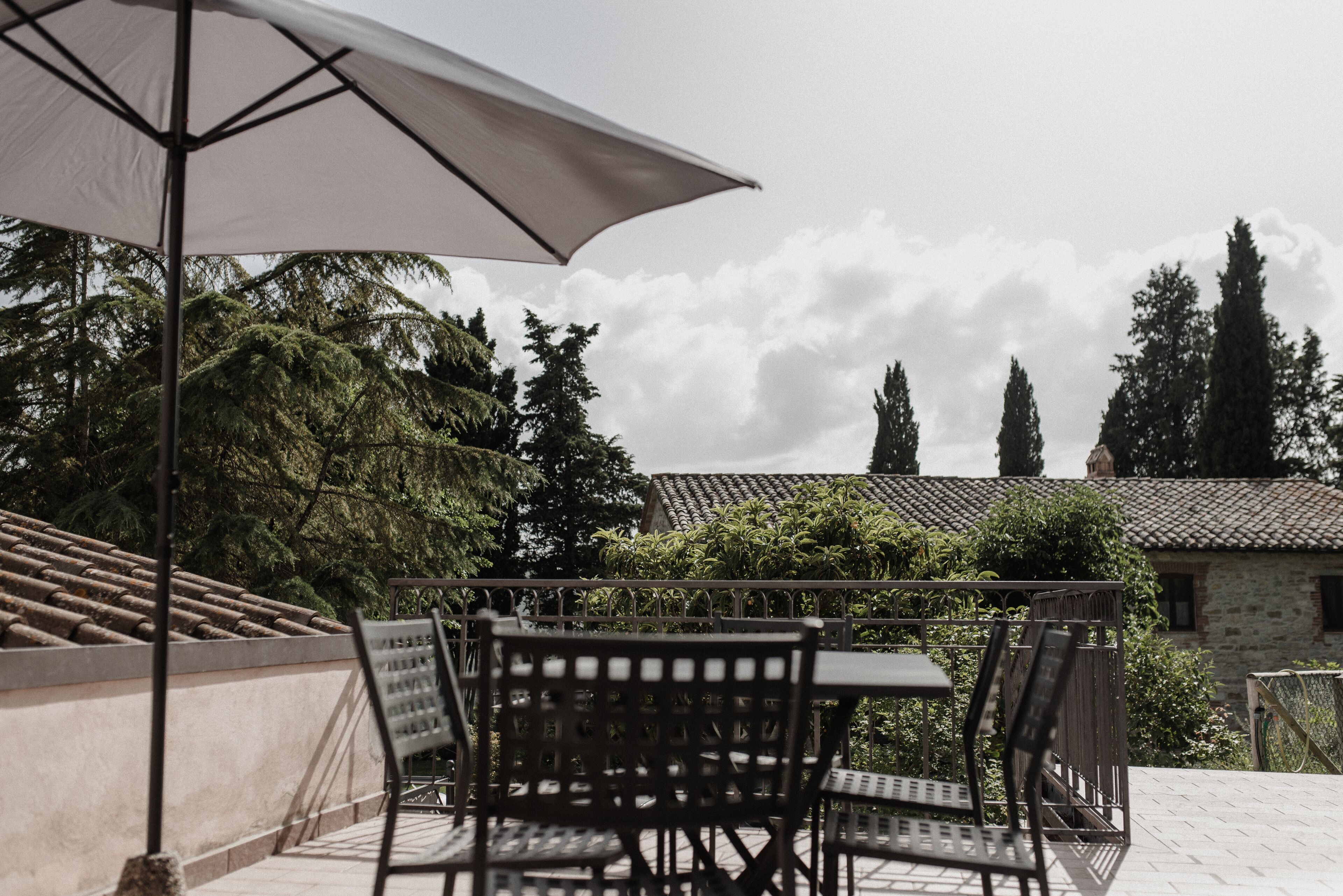 Una terrazza con tavolo e sedie, un ombrellone e vista su alberi ed edifici.
