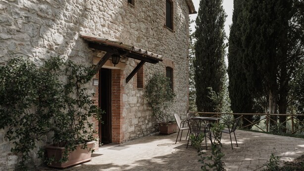 Un edificio rústico de piedra con puerta de madera y un pequeño patio con mesa y sillas.