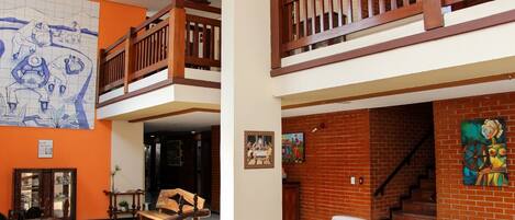 Un intérieur spacieux avec un plafond haut, des balustrades en bois sur le balcon, une grande fresque murale et un escalier menant à un niveau supérieur.
