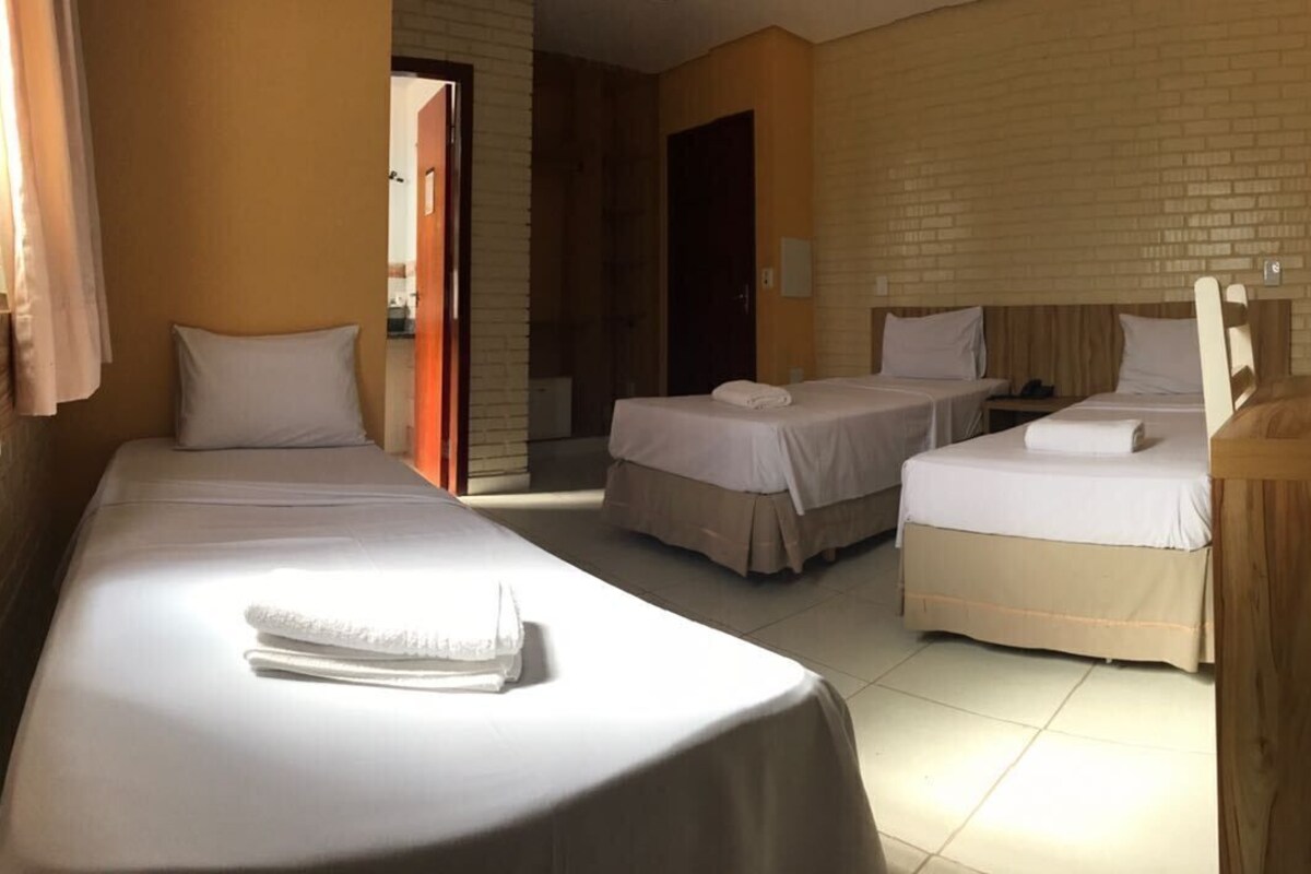 A hotel room with three beds, a wooden desk, and a brick wall.