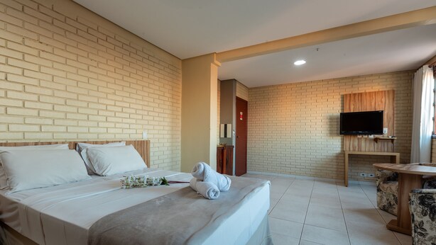 Een hotelkamer met een bakstenen muur, een bed met witte lakens, een televisie op een houten standaard en een kleine ronde tafel.