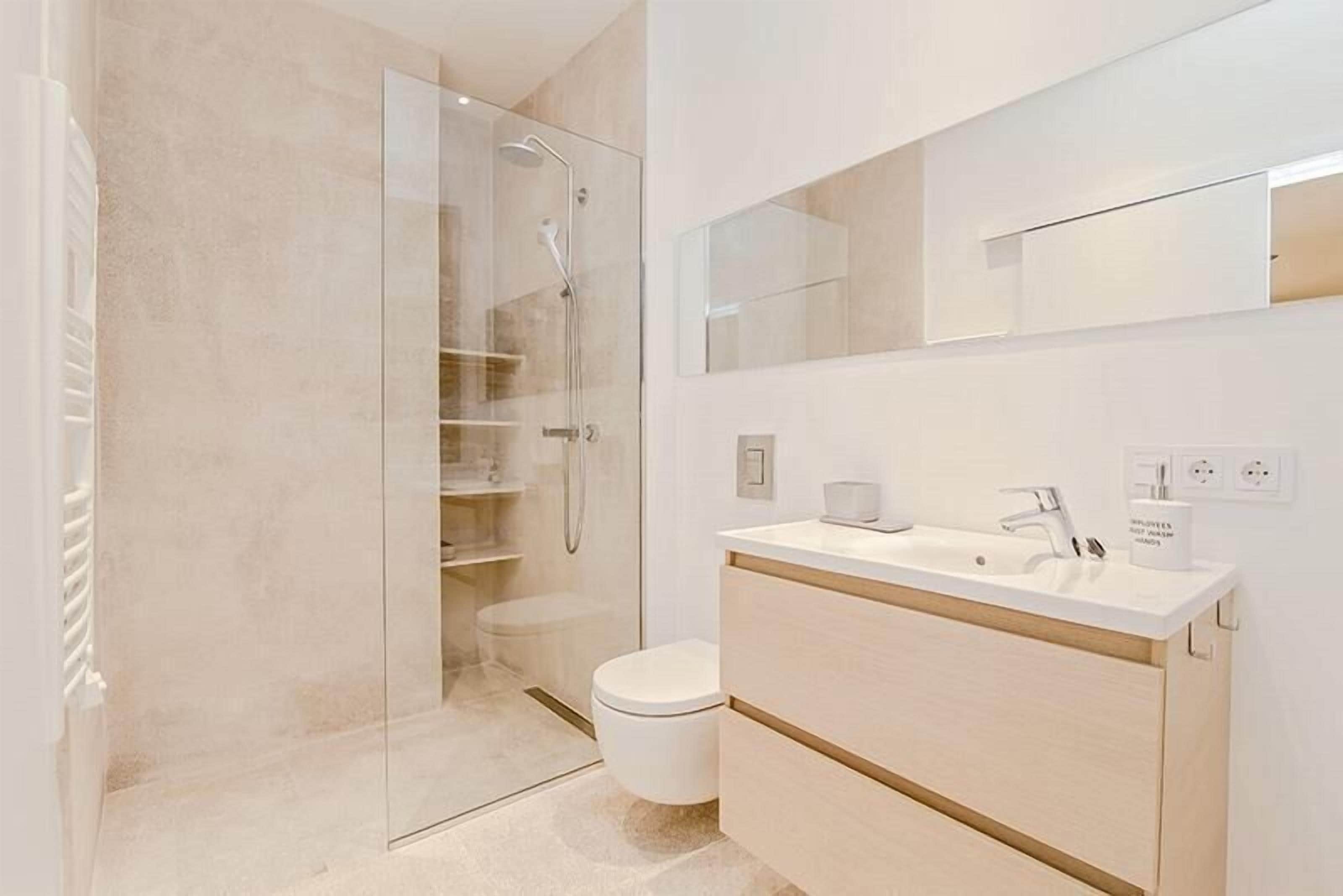 Een moderne badkamer met een douchecabine van glas, een toilet en een wastafel met spiegel.