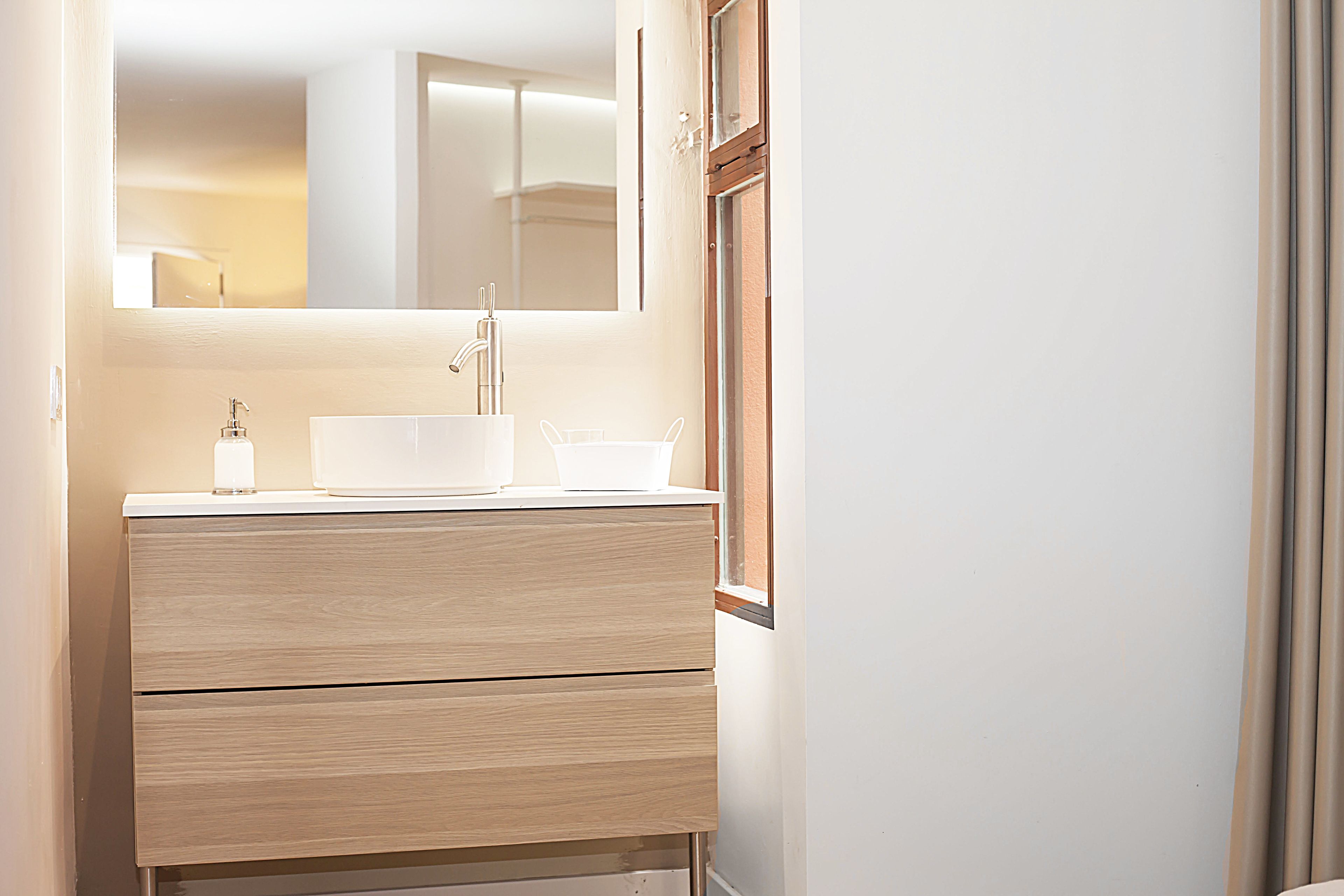 Un baño con un lavamanos blanco, un espejo encima y un mueble de madera debajo.