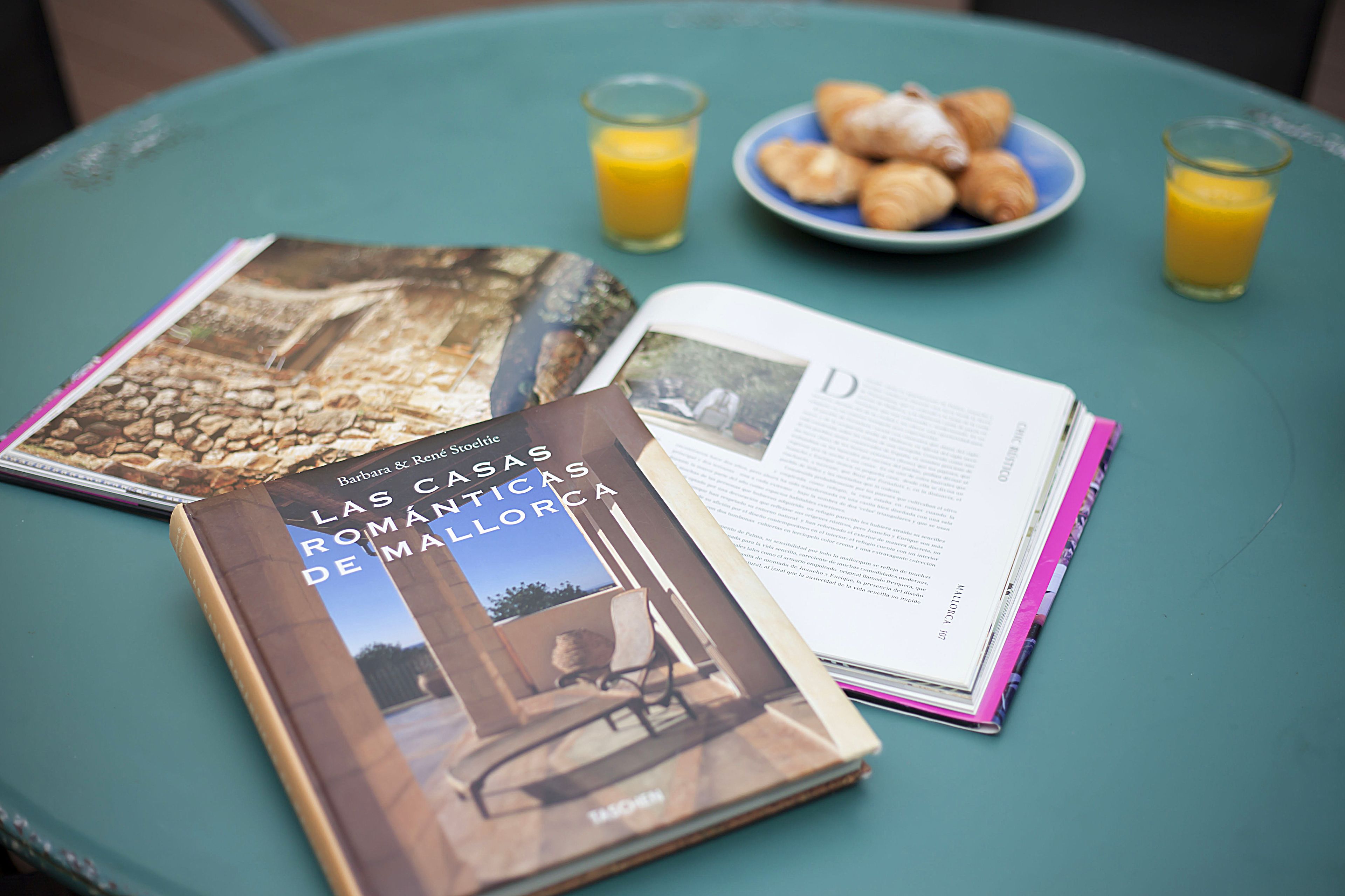 Una mesa con un libro, un plato de cruasanes y dos vasos de zumo de naranja.
