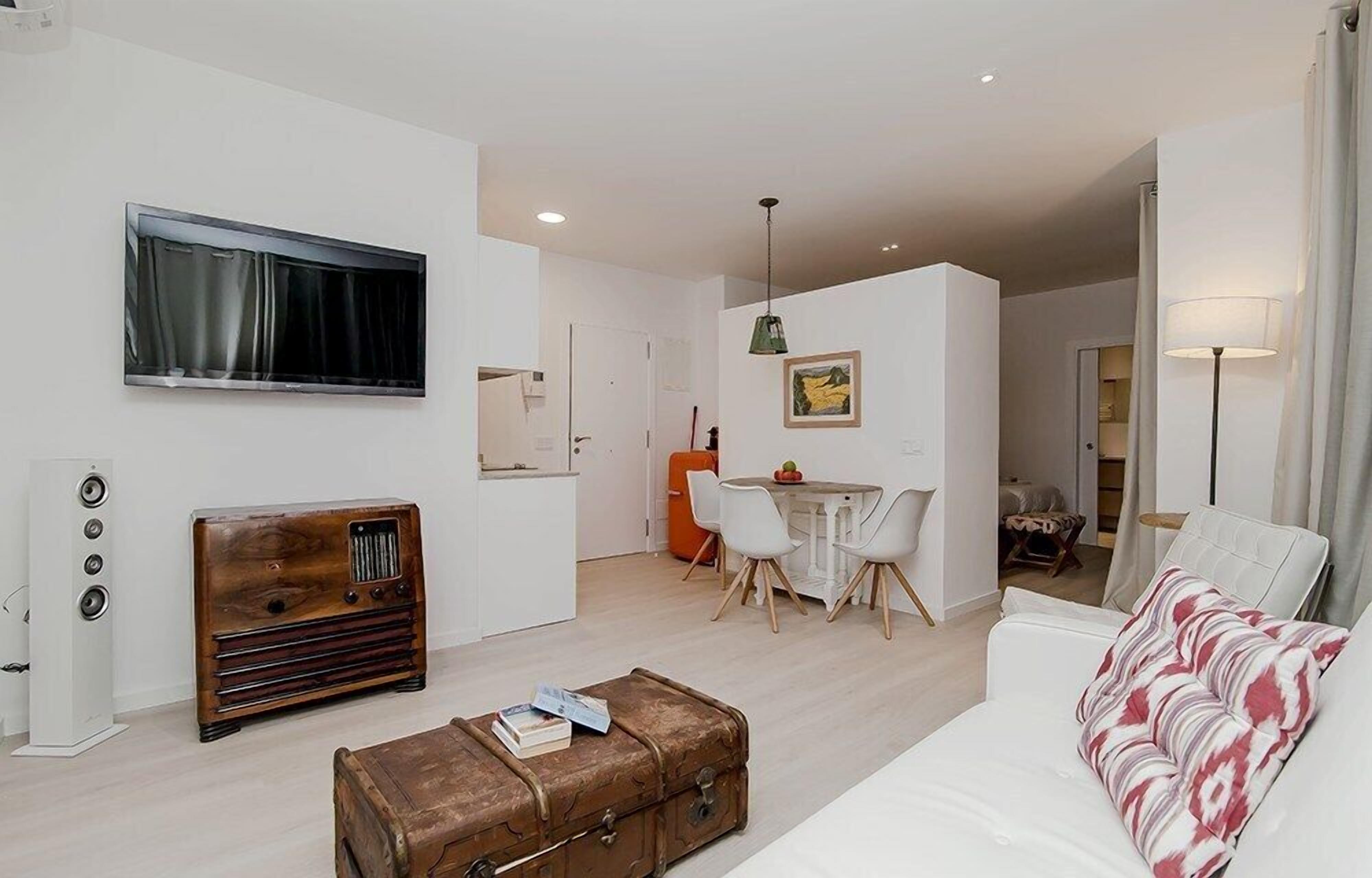 Un salon moderne avec un canapé blanc, une radio ancienne, une commode en bois et un coin repas comprenant une table et des chaises.