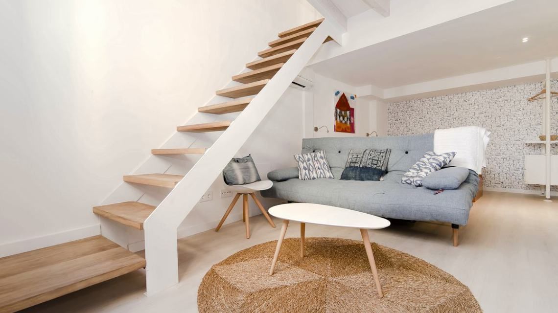 Ein modernes Wohnzimmer mit Treppe, einem grauen Sofa und einem runden Teppich.
