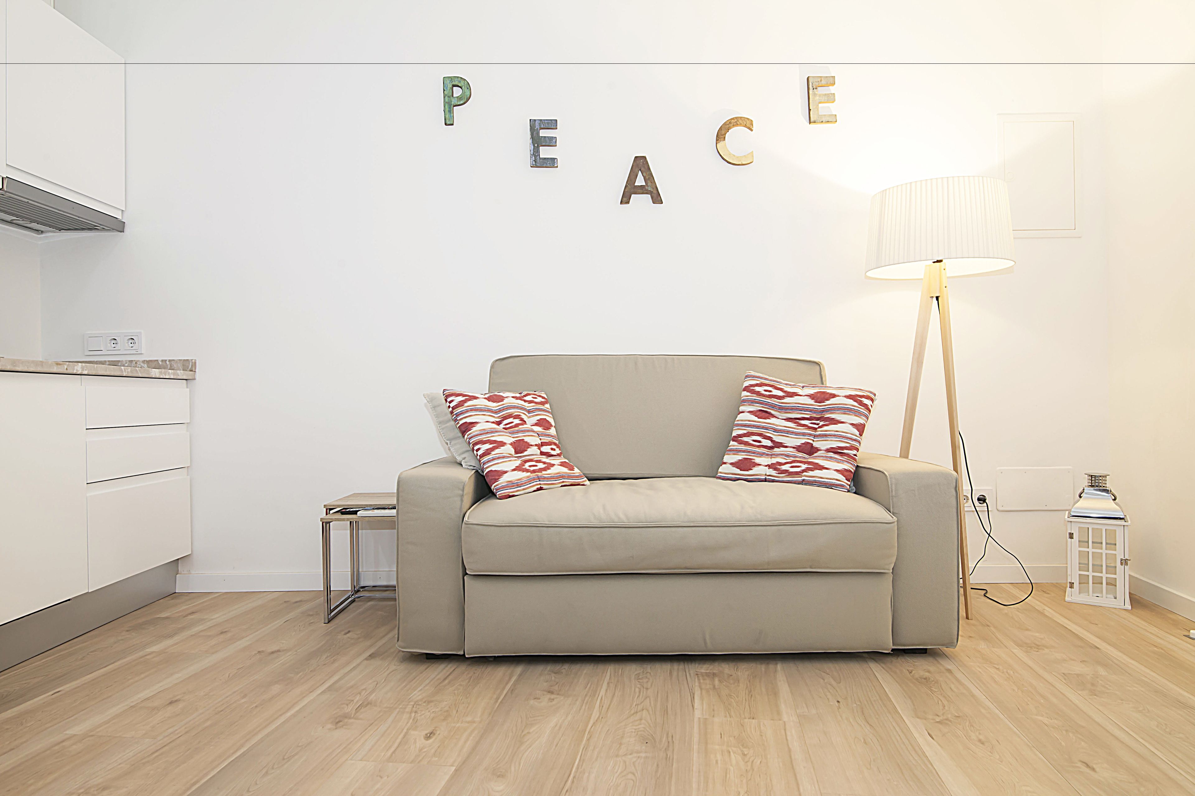 A modern living room with a beige sofa, patterned pillows, a floor lamp, and a wall with the word "PEACE" spelled out.