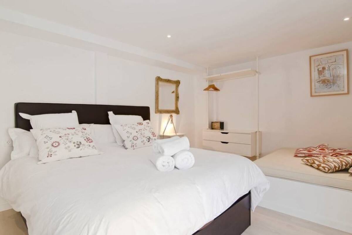 Un dormitorio con una cama grande, una mesita de noche, una lámpara colgante, un espejo y una obra de arte en la pared.