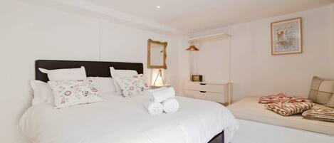 A bedroom with a large bed, a bedside table, a hanging light, a mirror, and a wall-mounted artwork.