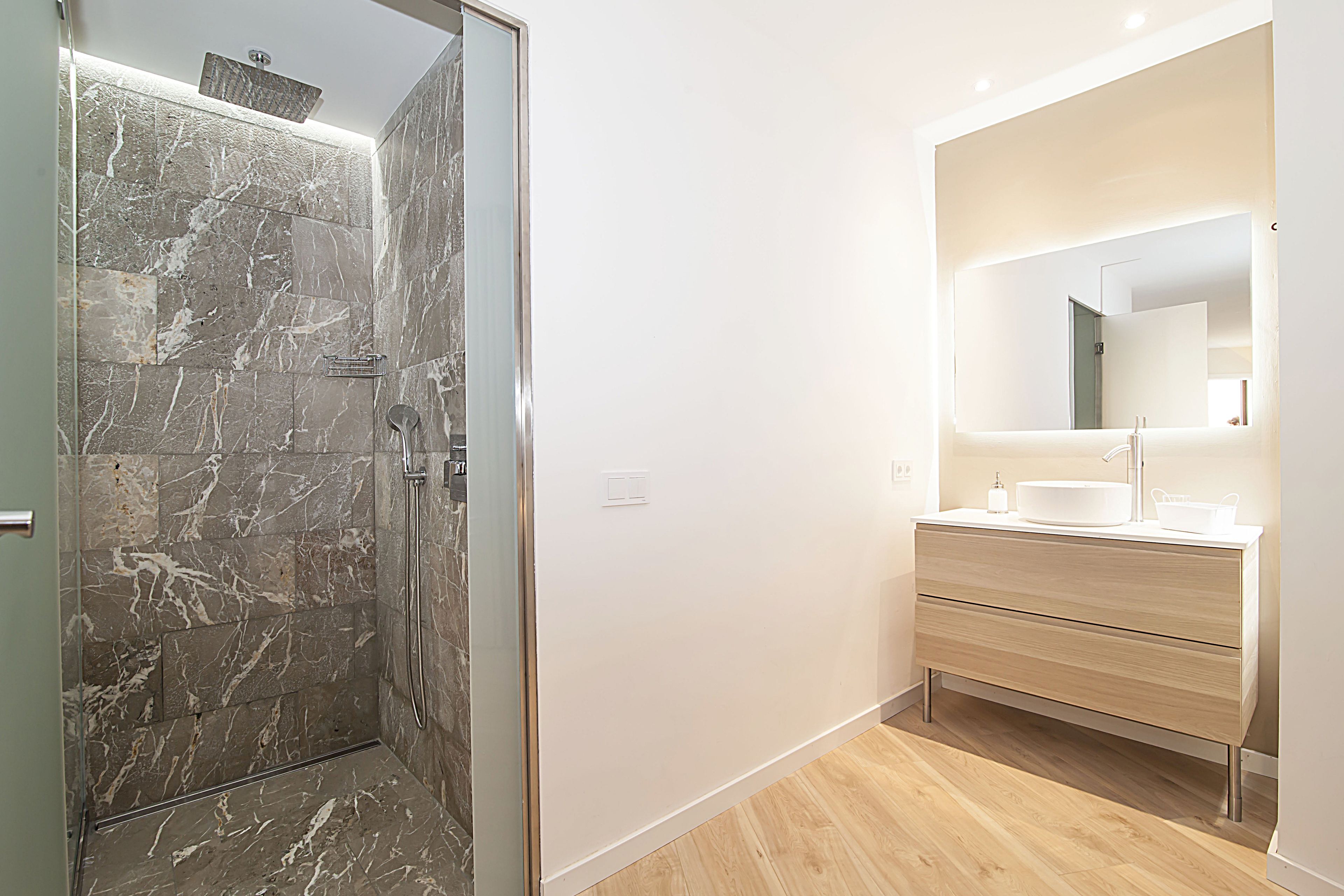 A modern bathroom with a marble shower, a large mirror, and a wooden vanity.