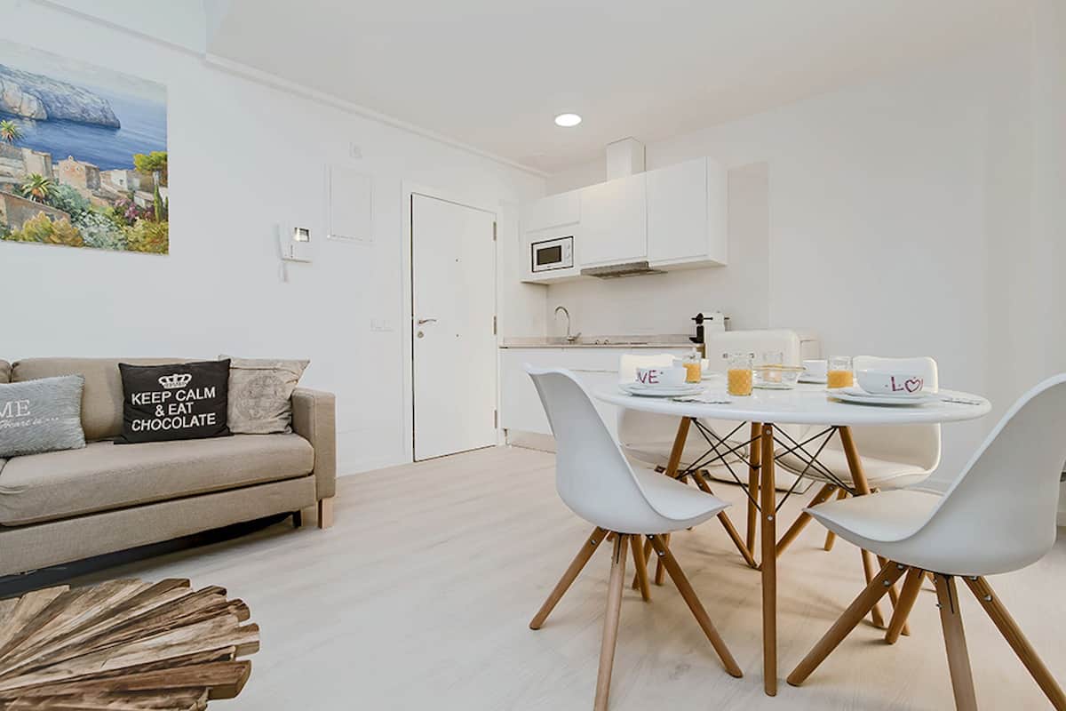 Una sala moderna con comedor, un sofá con cojines, una mesa de centro y una cocina con microondas.