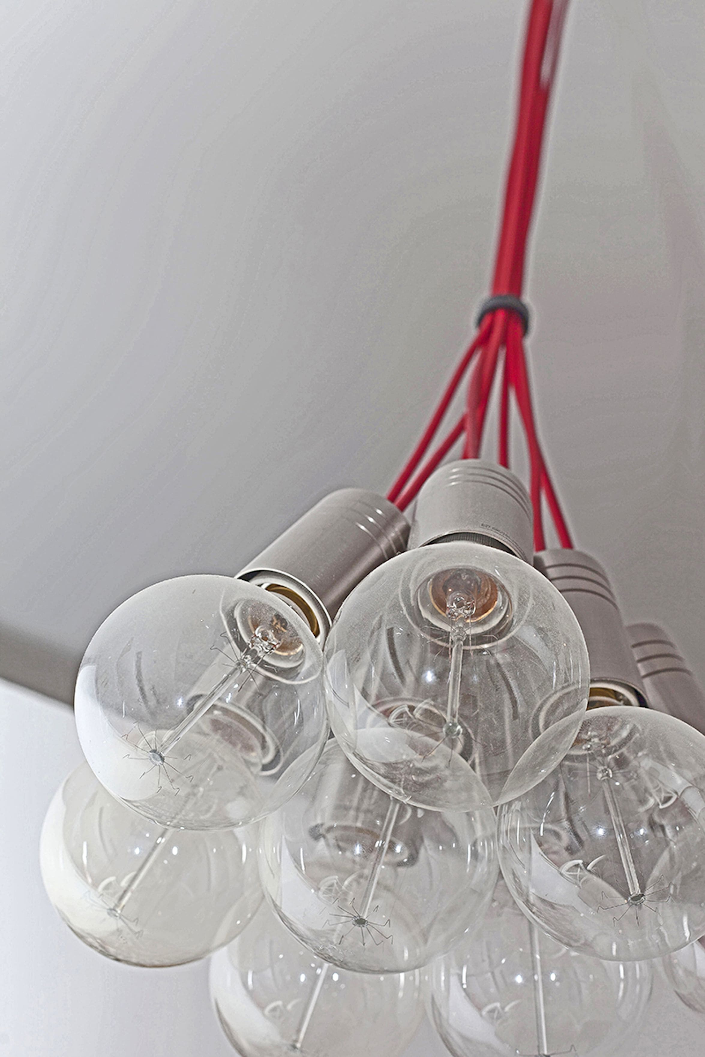 Un ensemble d’ampoules en verre transparent, dont on peut voir les filaments et les fils rouges, qui font probablement partie d’un luminaire.