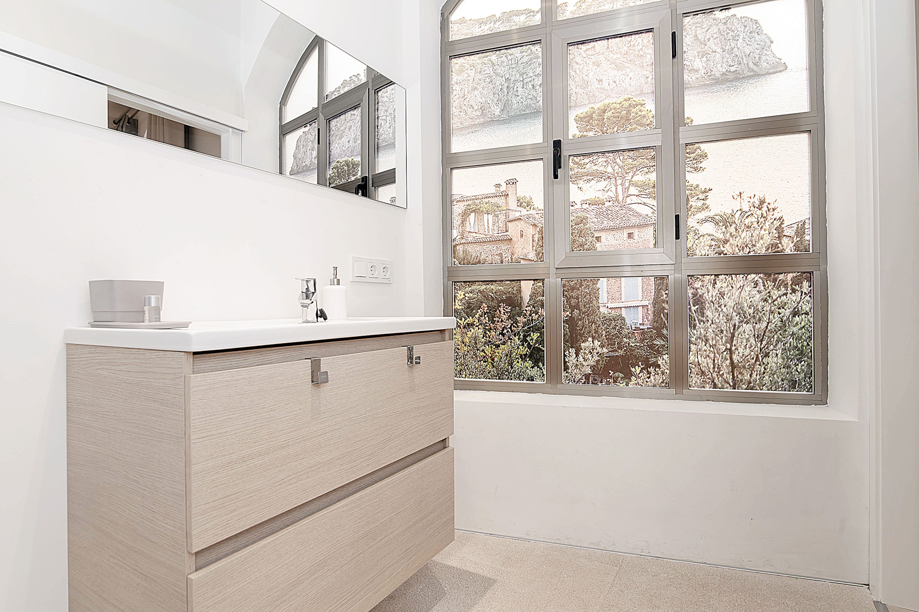 A modern bathroom with a white vanity, a large mirror, and a view of a building through a window.