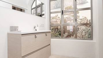 A modern bathroom with a white vanity, a large mirror, and a view of a building through a window.