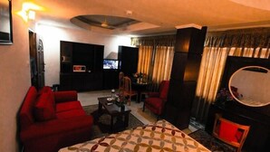 Quarto de hotel com cama, sofá vermelho, mesinha com um vaso, televisão e lareira.