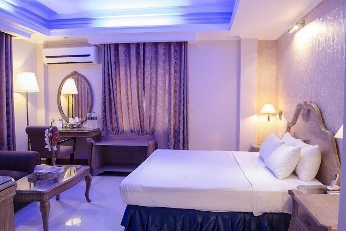 A hotel room with a bed, a desk, a chair, and a lamp.