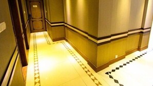Um corredor de hotel com padrão de piso xadrez, um balcão de recepção de madeira e uma escada que leva a outro andar.