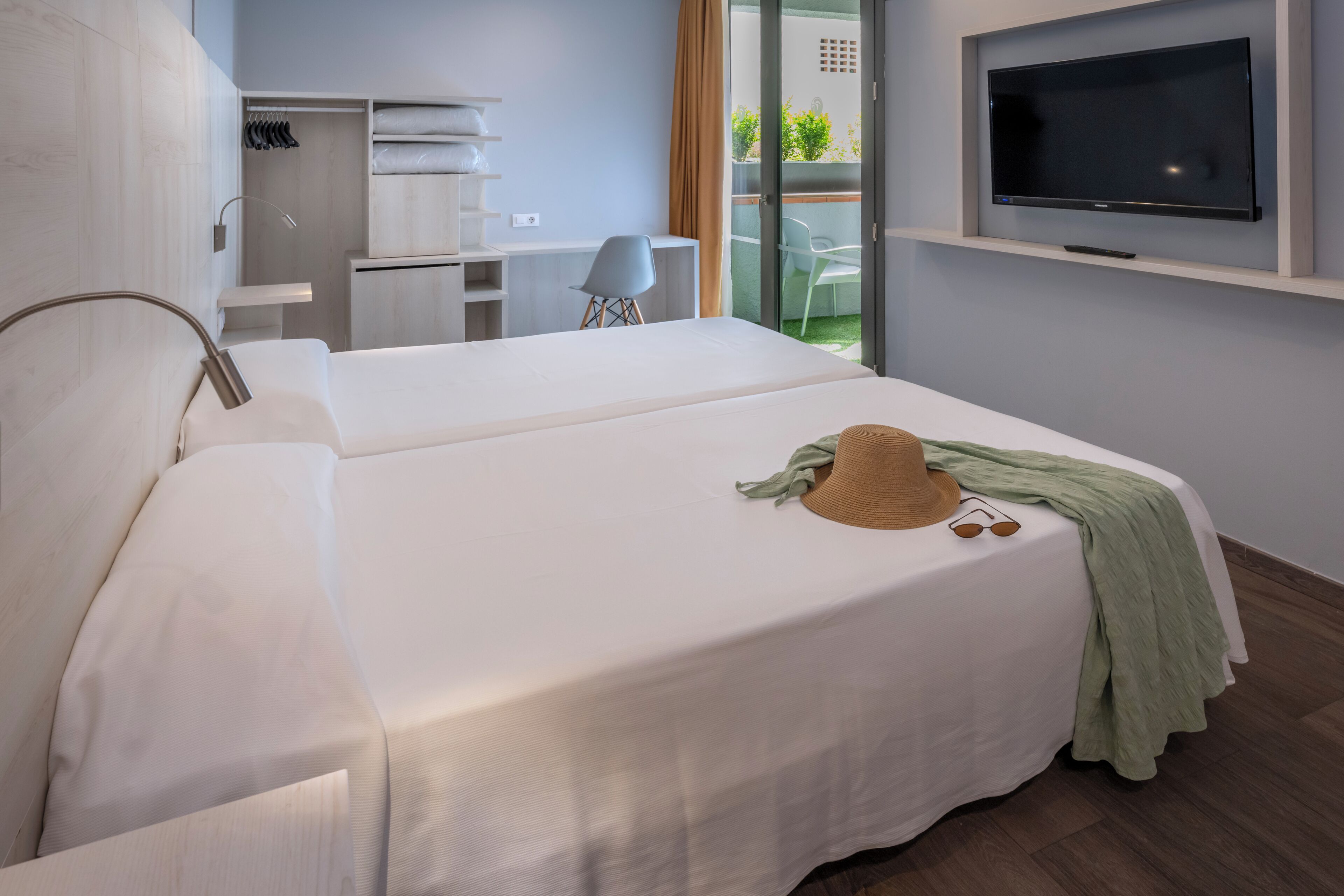 Habitación de hotel con cama, escritorio, silla, televisor y balcón con vistas.