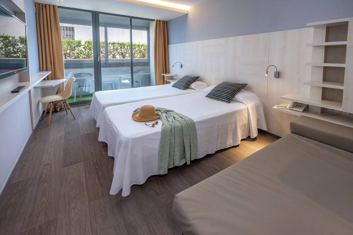 Habitación de hotel con dos camas, un escritorio, una silla y vistas al exterior.