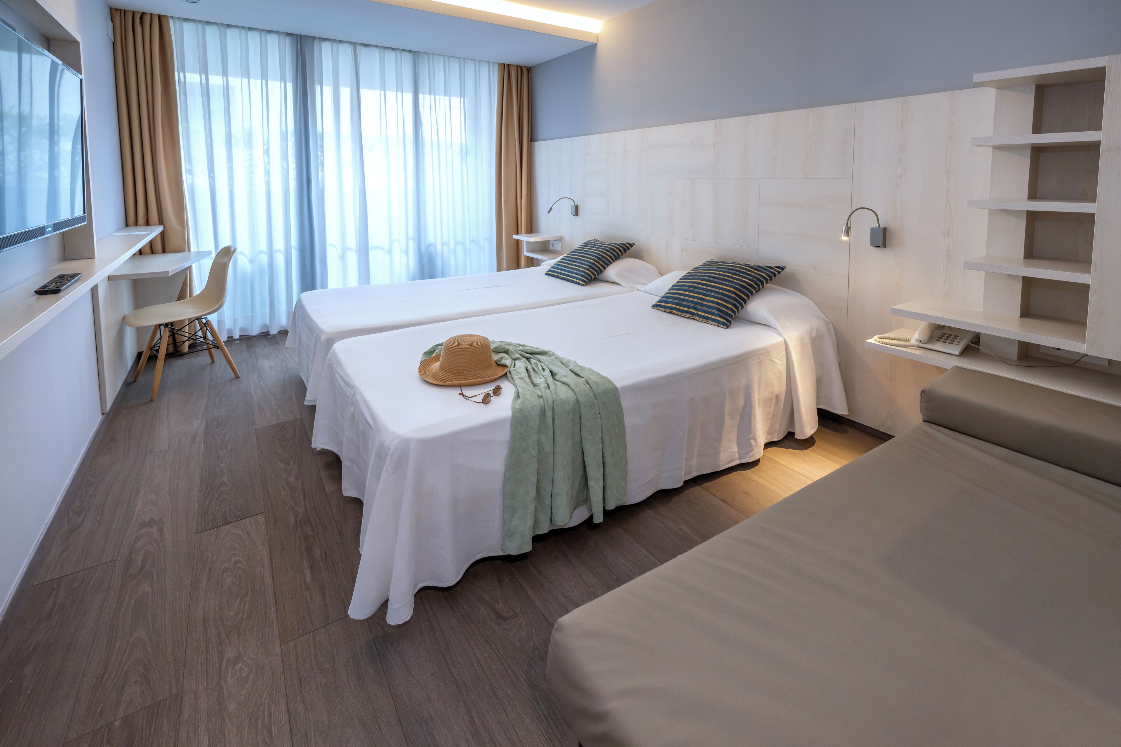 Habitación de hotel con dos camas, un escritorio, una silla y un televisor.
