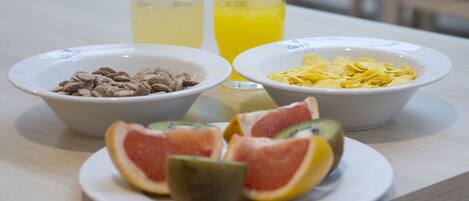 A breakfast table with bowls of cereal, a plate of sliced fruit, and two glasses of orange juice.