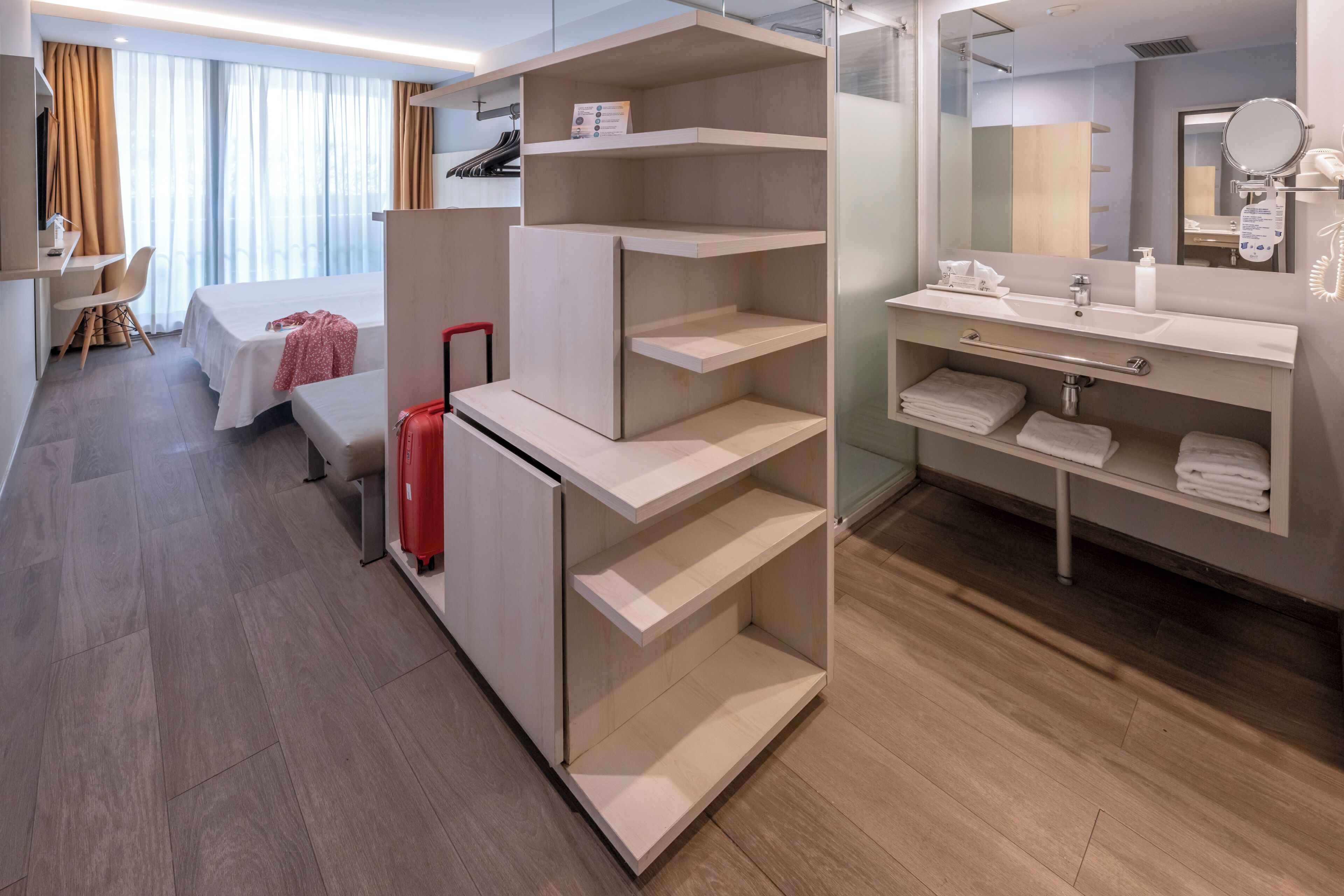 Una habitación de hotel con cama, escritorio, silla y una maleta roja.