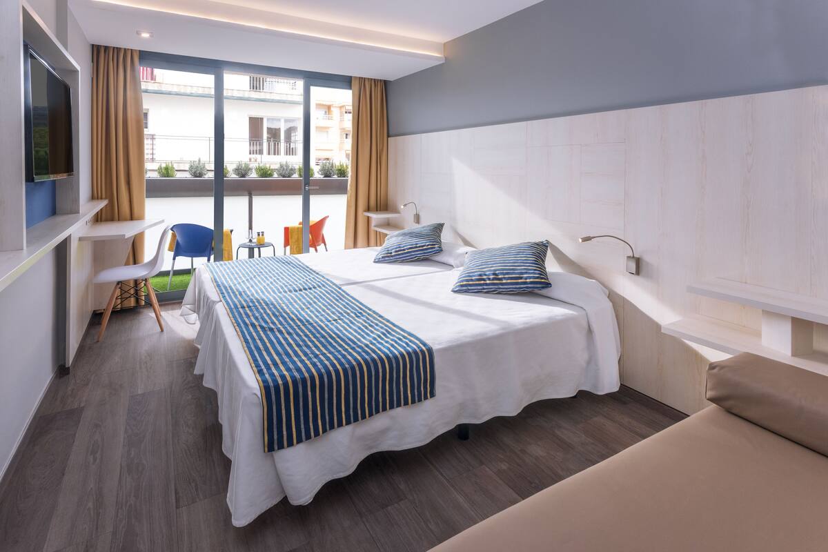 Habitación de hotel con una cama grande, televisión, escritorio con silla y vistas al balcón exterior.