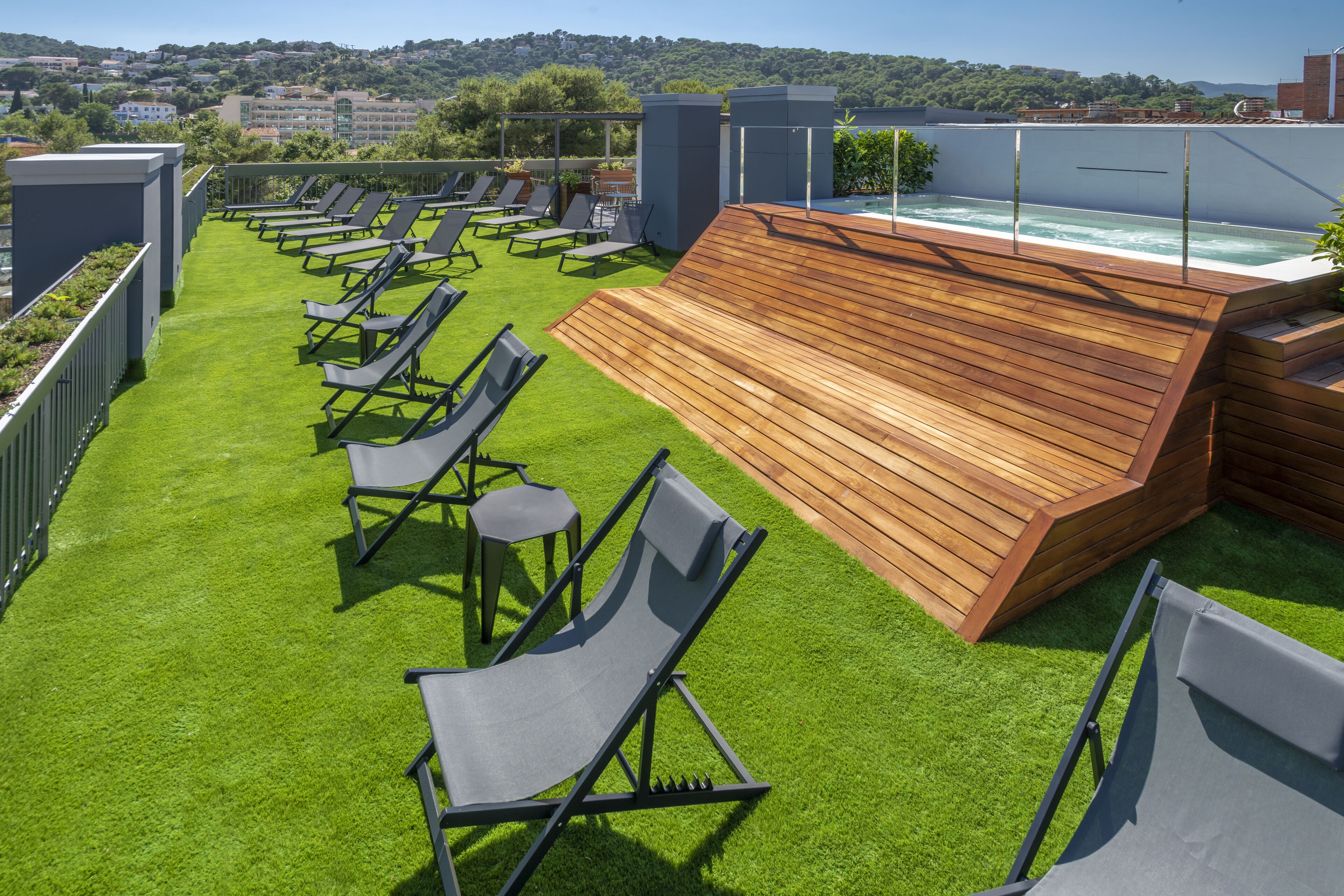 Una terraza en la azotea con jacuzzi, césped artificial verde y tumbonas.