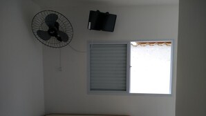 A room with a ceiling fan, a closed window with blinds, and a small table. - Consulado Praia Hotel (Guarujá)