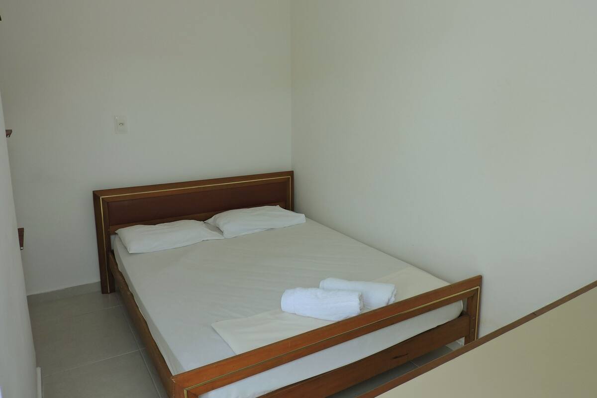 A single bed with a wooden frame, white bedding, and two rolled towels on the bed.