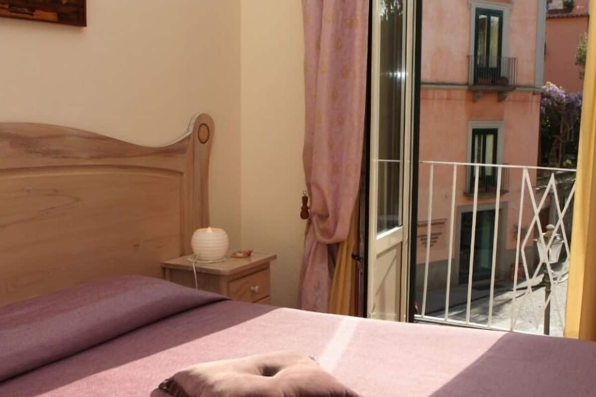 A bedroom with a wooden headboard, a bedside table with a lamp, and a view of a balcony with a railing.