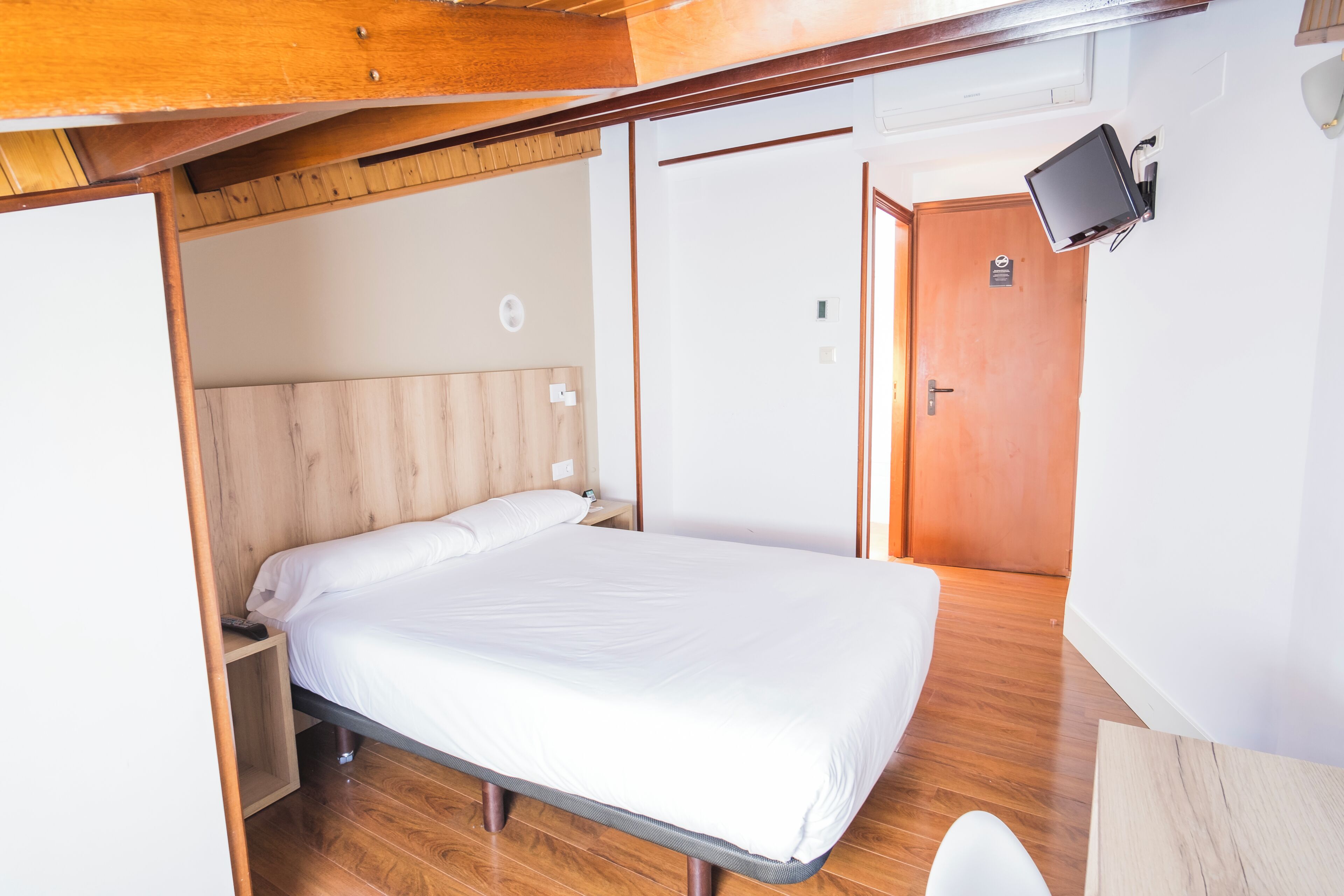 Una cama individual con cabecera de madera en una habitación con suelo de madera y una mesita de noche pequeña.