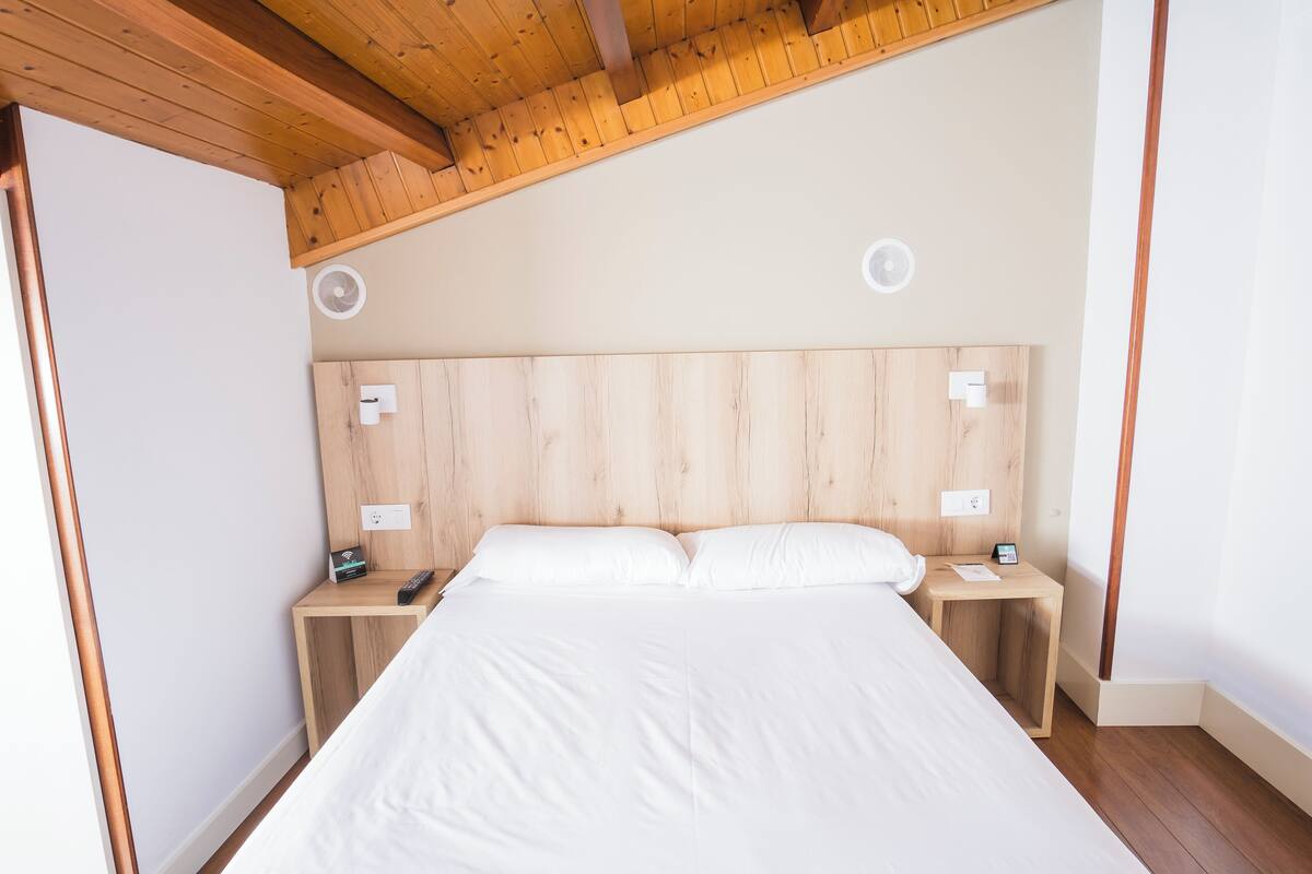 Een slaapkamer met een houten hoofdeinde, een bed met witte lakens, twee nachtkastjes met lampen en een plafondventilator.