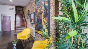 Un vestíbulo con una escalera, una silla amarilla, una planta en maceta y un cuadro grande en la pared.