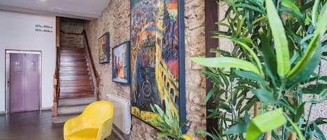 A lobby with a staircase, a yellow chair, a potted plant, and a large painting on the wall.