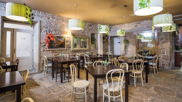 Un restaurante con paredes de piedra, varias mesas y plantas colgantes.