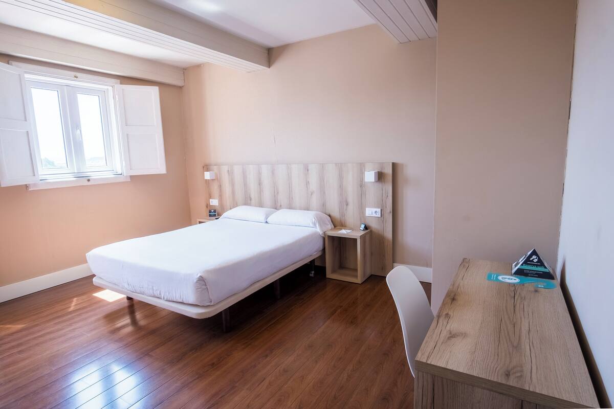 Een slaapkamer met een bed, nachtkastjes, een bureau en een raam.