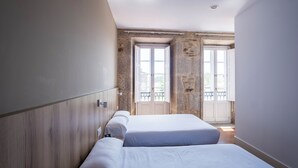 Un dormitorio con dos camas, una pared de piedra y una puerta al balcón.