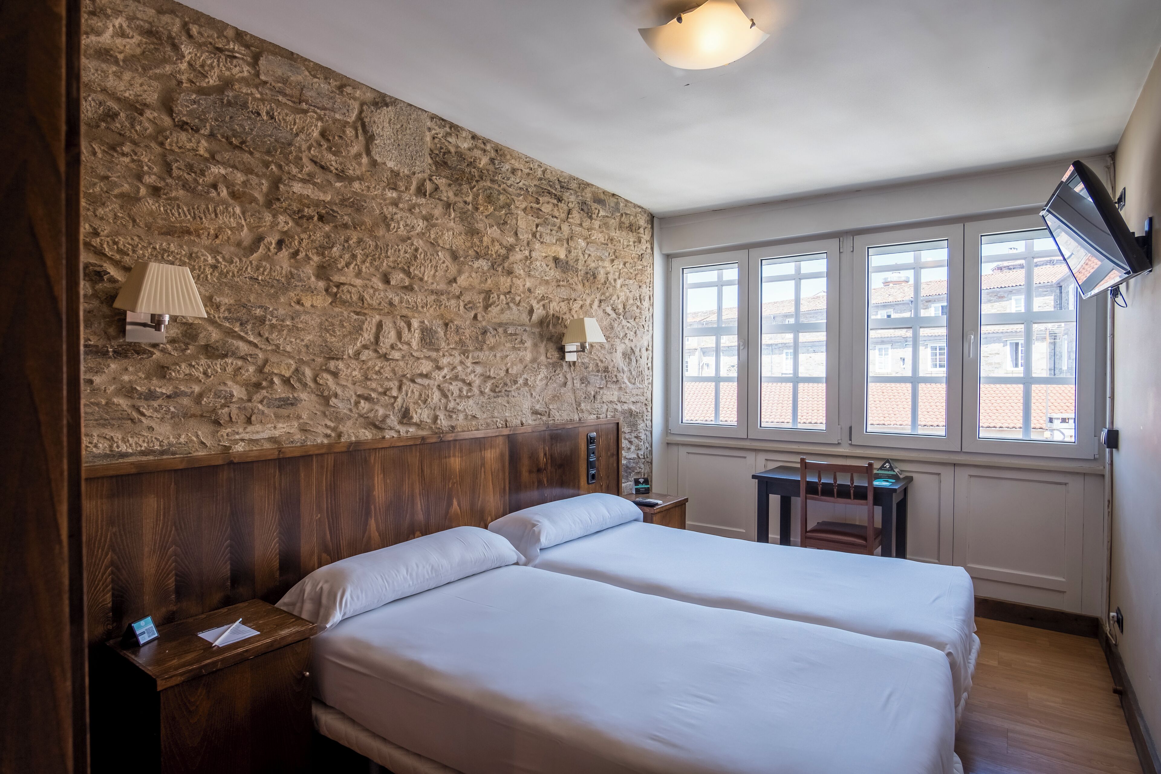 A room with two beds, a stone wall, a wooden headboard, a desk, and a chair.