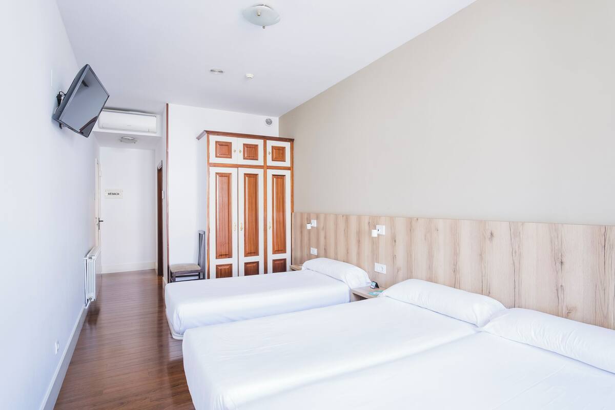 Hotelkamer met twee bedden, een houten hoofdeinde, een aan de muur bevestigde televisie en een deur naar een badkamer.