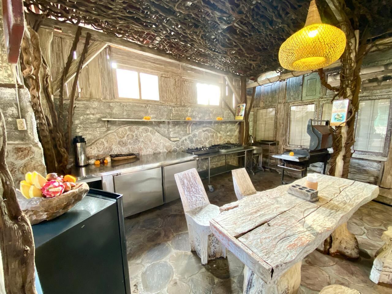 A rustic kitchen with a stone countertop, a wooden dining table, and a hanging light fixture.