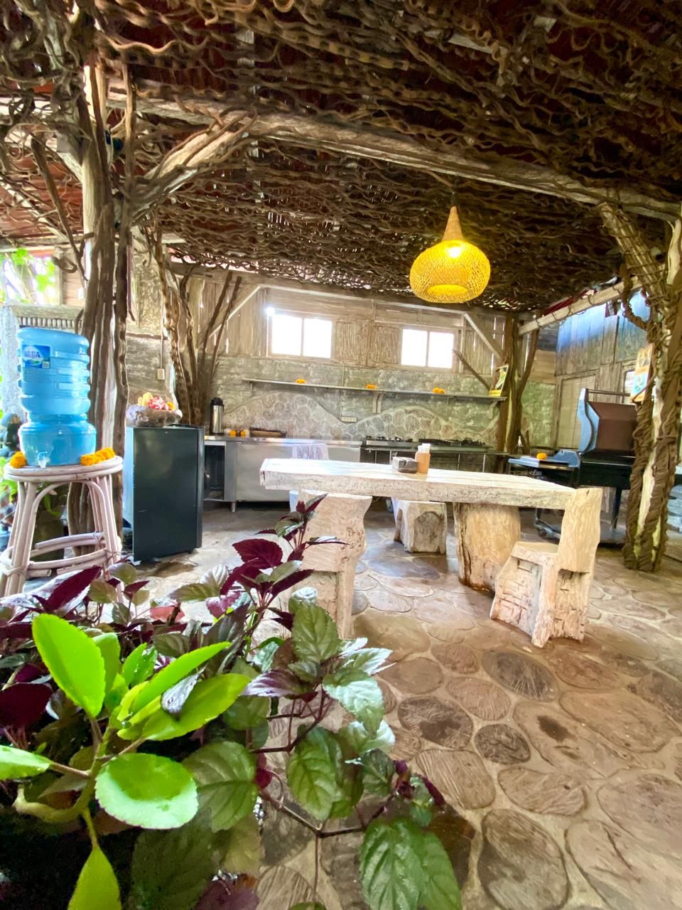 A rustic kitchen with a stone floor, wooden furniture, and a hanging light fixture.