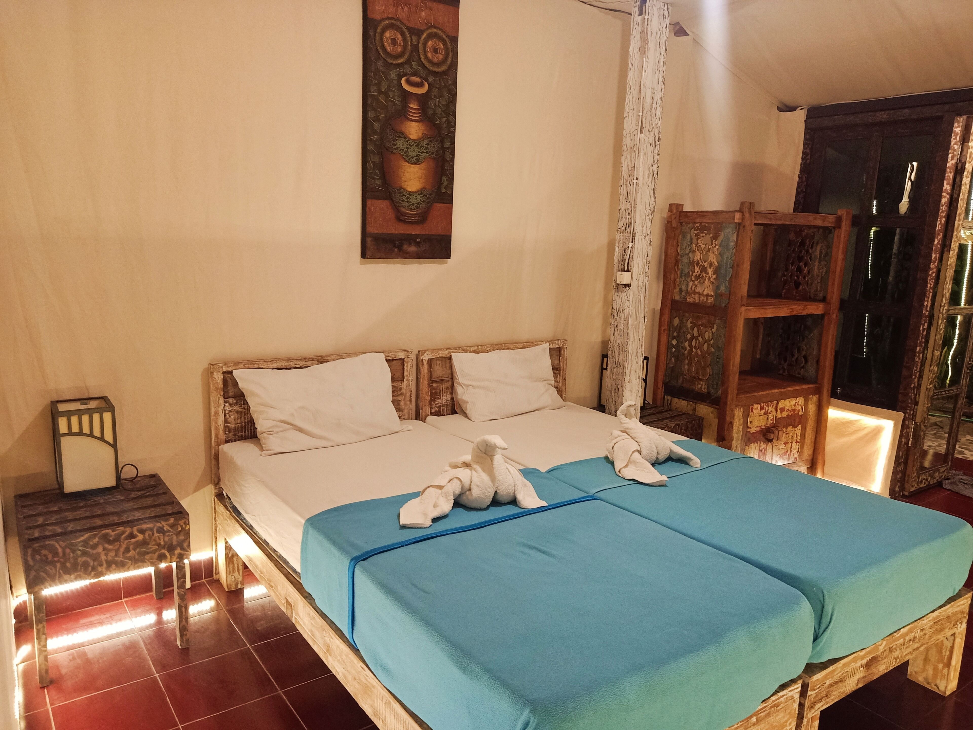 Uma cama de casal com colcha azul, travesseiros brancos e duas toalhas sobre a cama.