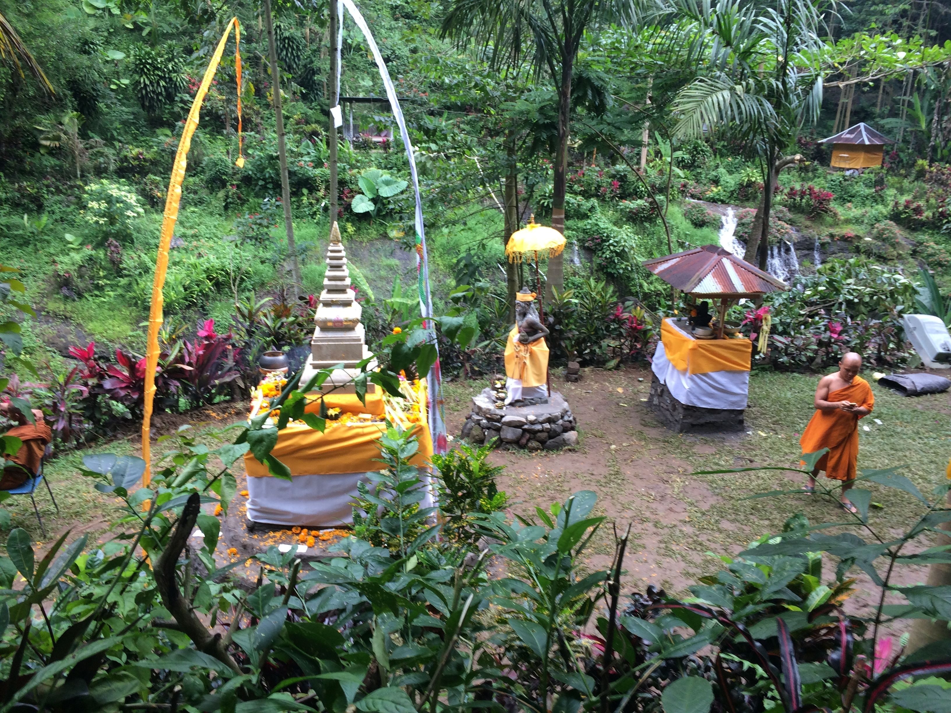 A serene garden with a statue, a small shrine, and a monk.