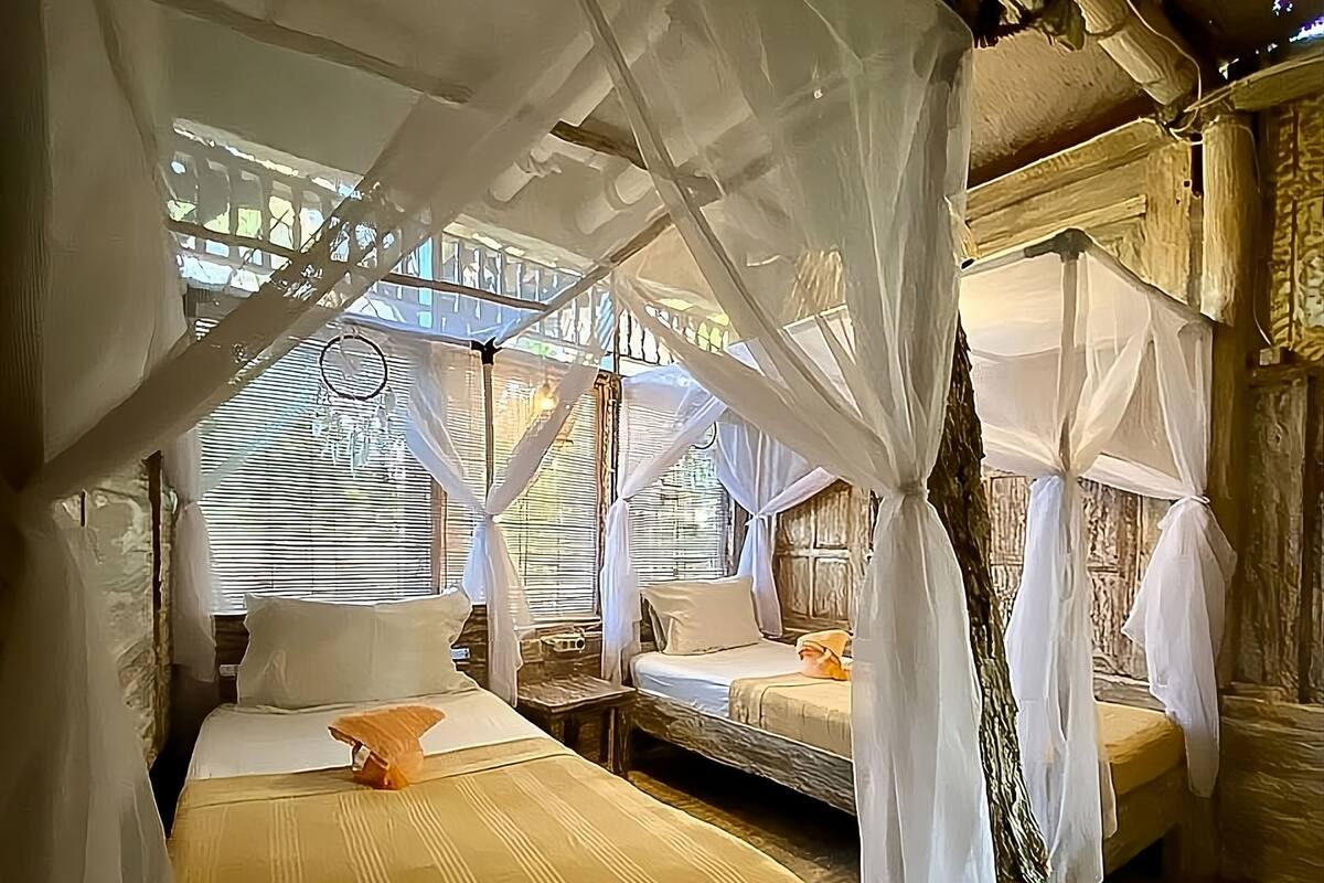 A room with two beds, each covered with white mosquito nets, and wooden furniture.